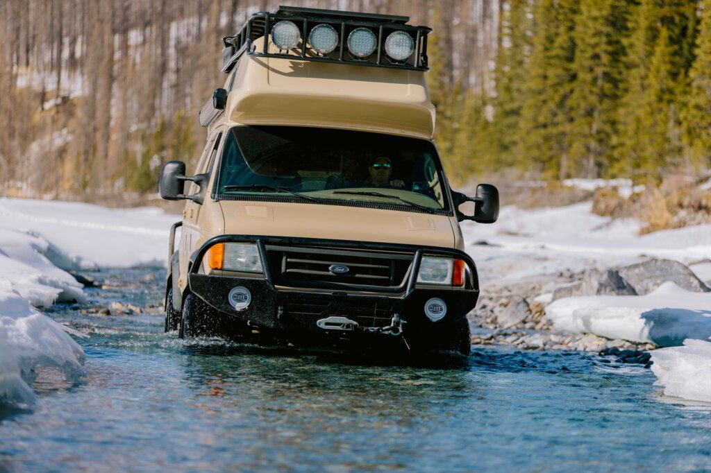 A beige Ford E-Series van crossing a river.